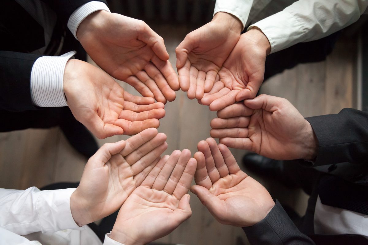 Team people join hands in circle palms up as concept of care protection, contribution in growing business and startup growth, enganing crowdfunding, unity, trust or safety concept, close up top view